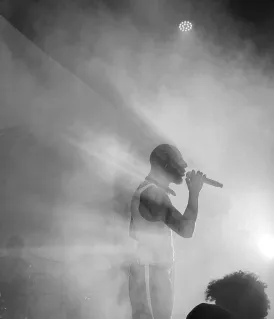 Artiste en silhouette chantant avec un microphone sous un éclairage intense et des effets de fumée en noir et blanc.