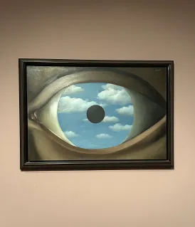 Peinture encadrée représentant un œil humain avec un ciel bleu et des nuages visibles à travers l'iris et une pupille noire au centre.